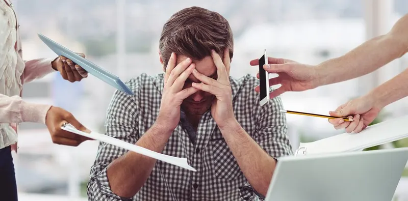 An overwhelmed person holding their head while being expected to do several things at once.