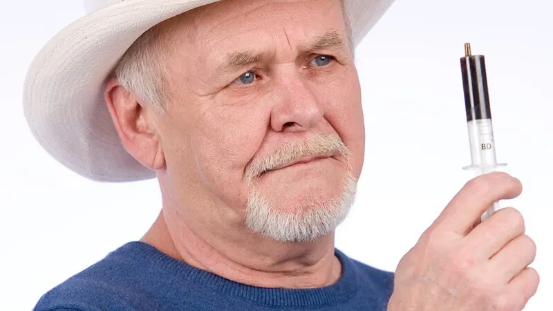 A person wearing a hat and holding a small syringe.